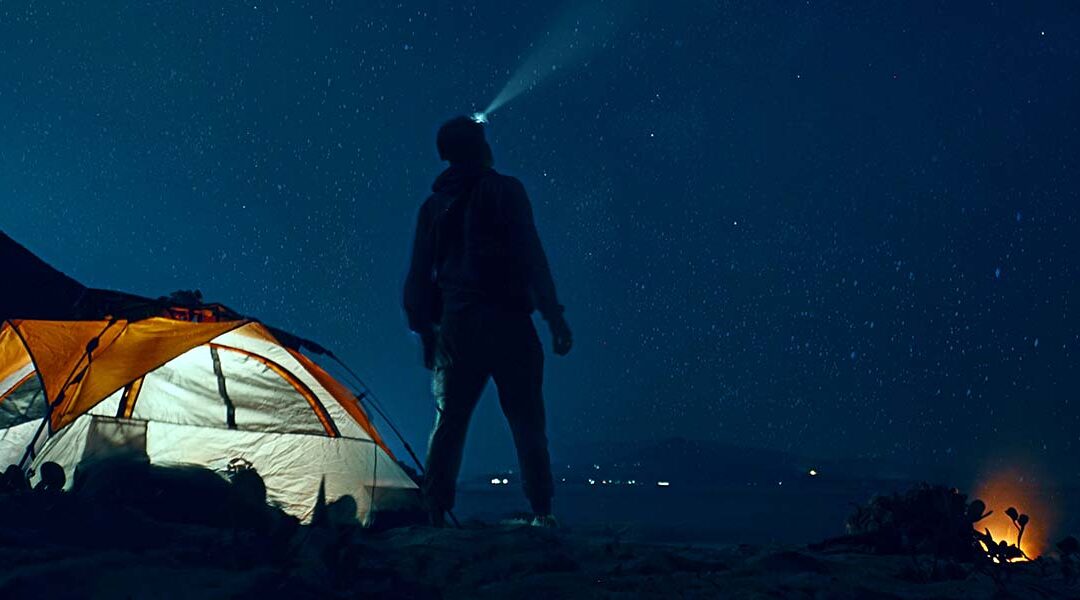 Man camping at night with sky full of stars.